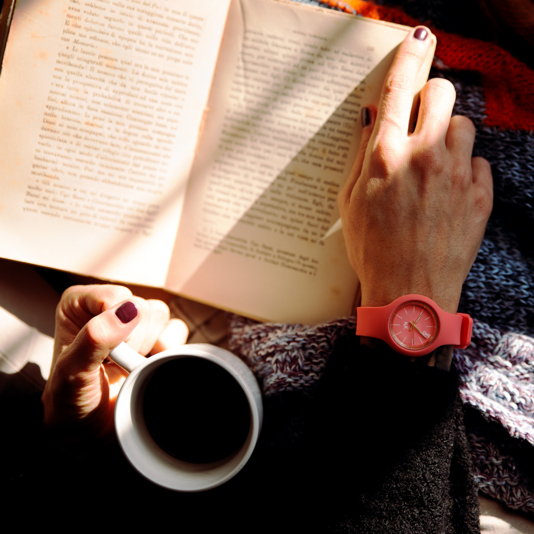 looking down at a book someone is reading. They have a blanket on their lap and a cup of hot drink