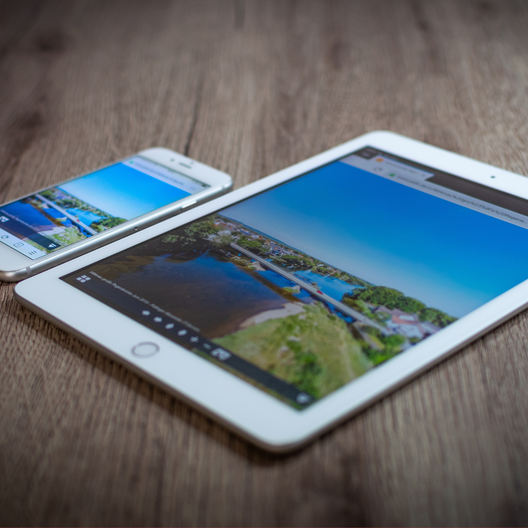 white iphone and white ipad on a wooden tabletop . Both have a browser window open to a bridge 