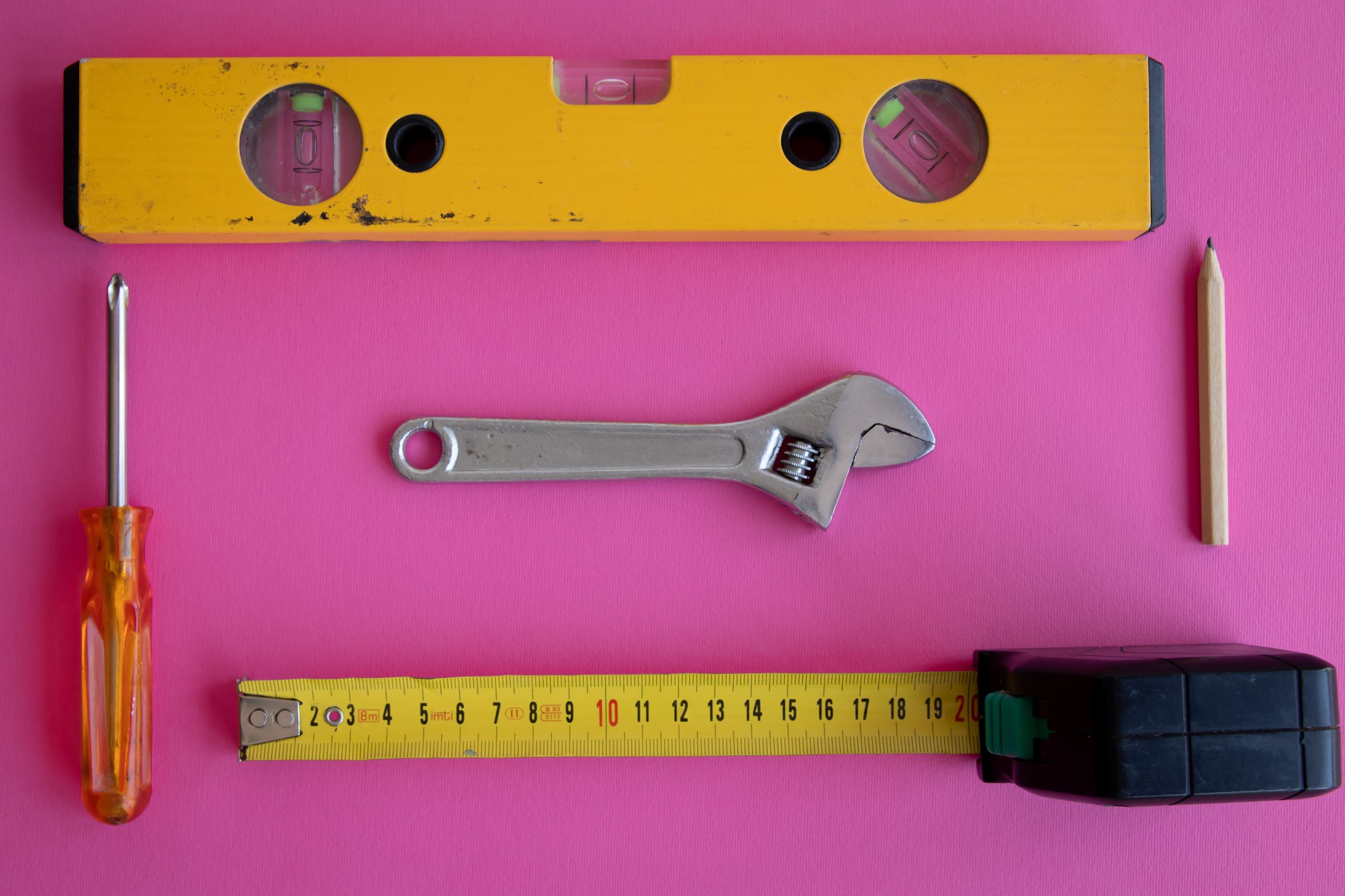 Carpentry Tools on a Pink Surface: leveler, pencil, measuring tape, tool, phillips head screwdriver