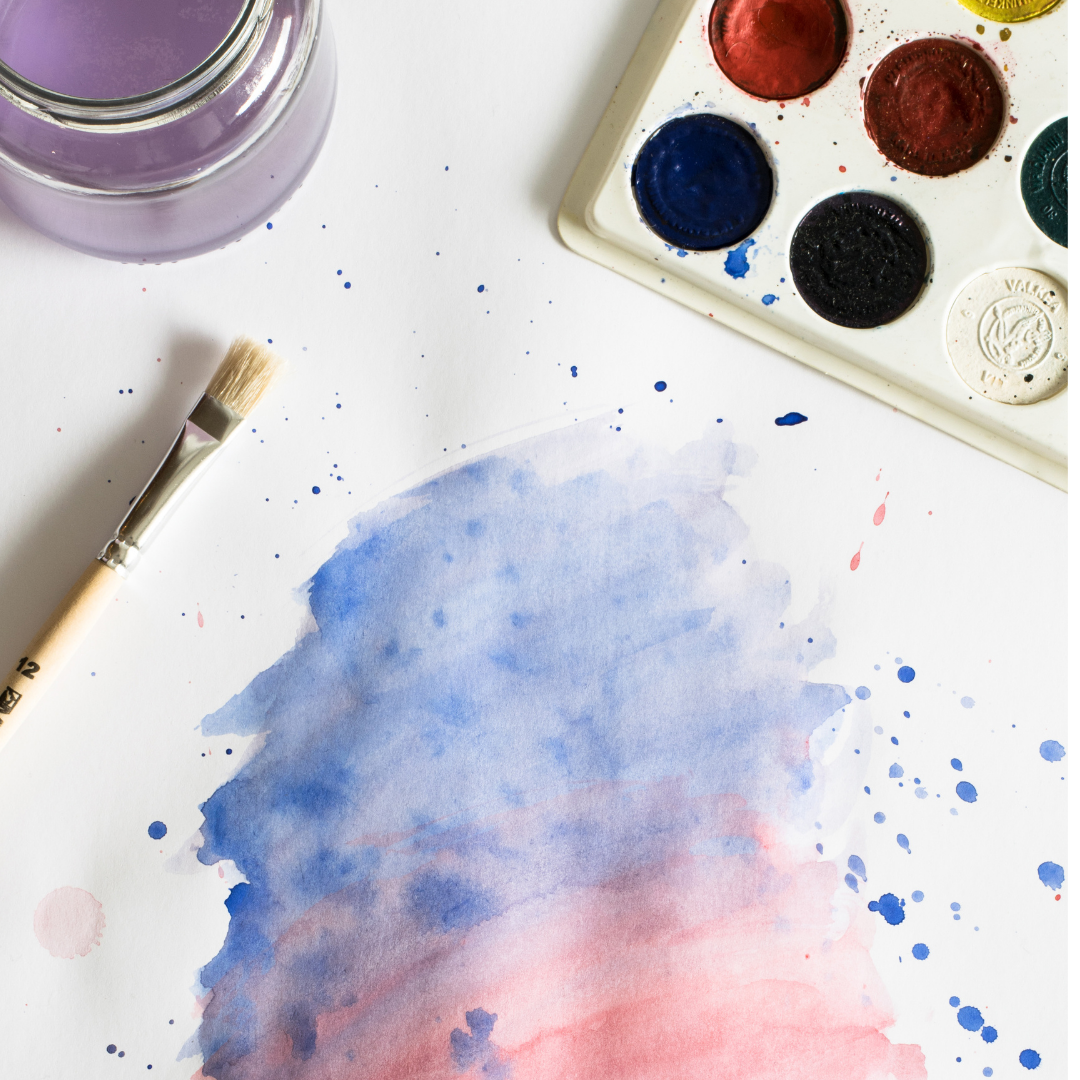 photo of paper with blue and pink watercolor, jar of water, paintbrush and paints