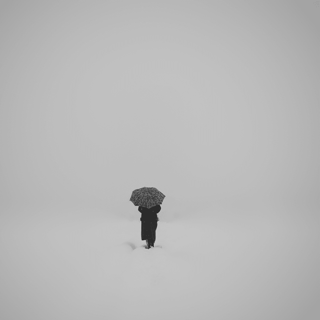 Person standing alone in snow, holding an open umbrella. Very desolate looking black and white photo