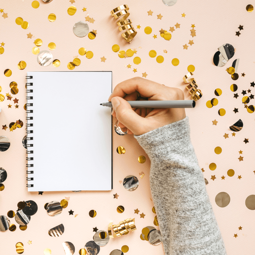 arm holding pen over a blank sheet of paper with shiny ribbon and stars scattered about