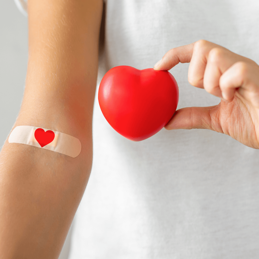 Person from shoulders to waist, arm has a bandaid with a heart on it, other hand holding a heart
