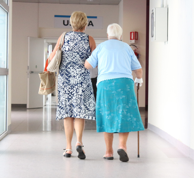 Woman helps an older woman using a walker down a hospital hallway